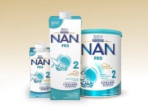 Valokuva: Nestlé NAN PRO 2 -maidonkorvikepakkaukset — pahvi, laatikko ja tölkki beigenvärisellä taustalla